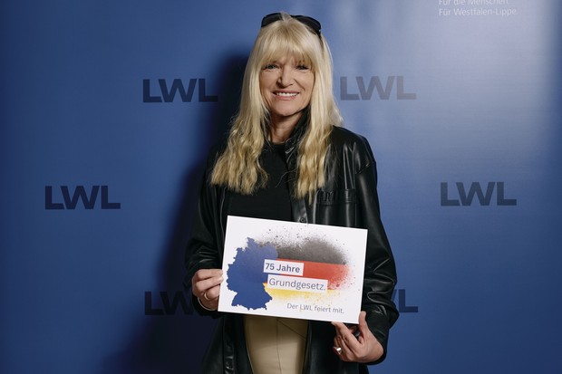 Portrait von LWL-Kulturdezernentin Dr. Barbara Rüschoff-Parzinger mit Schild in der Hand: "75 Jahre Grundgesetzt. Der LWL feiert mit."